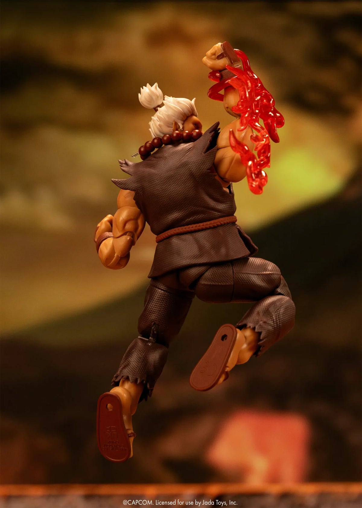 Figurine Akuma Ultra Street Fighter II Jada Toys en plein saut, vue de dos, avec un effet d’énergie rouge au bras levé